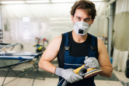 Mechanic male using machinery car polishers maintenance to remove marks repair. Portrait of muscular expert car paint technician in face mask holding car polisher to polish of car with refinement.の写真素材
