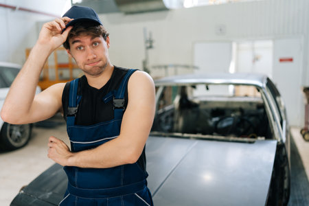 Portrait of wondering mechanic male in jumpsuit pensive looking at camera not knowing what disrepair during maintenance car in repair workshop. Doubtful repairman trying to solve problem in garage.の写真素材