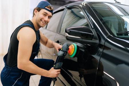 Portrait of positive mechanic male in uniform polish auto door using grinding unit in automobile repair and renew service station, smiling looking at camera. Concept of car repair and maintenance workの写真素材