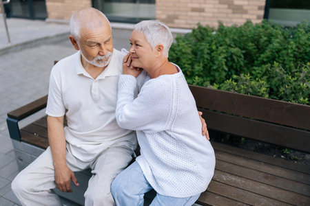 Portrait of beautiful happy elderly couple with gray-haired enjoying each other company sitting on urban bench on summer sunny warm day, showing affection and love after years of being together. Cの写真素材