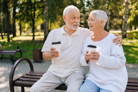 Affectionate senior couple savoring coffee in urban park on sunny summer day, sharing love and warmth, embracing and cherishing simple joys of life. Happy elderly people enjoying retirement together.の写真素材