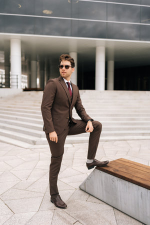 Full length vertical portrait of serious confident businessman in stylish suit and sunglasses posing outdoors, exuding success and professionalism, city architecture complementing modern urban look.の写真素材