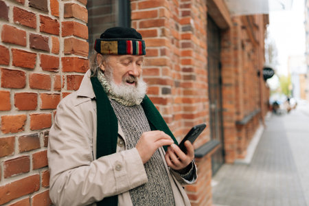 Medium shot portrait of aged man looking surprised using smartphone, standing on city street, reflecting hope and despair in urban isolation. Concept of unhappy retirement.の写真素材