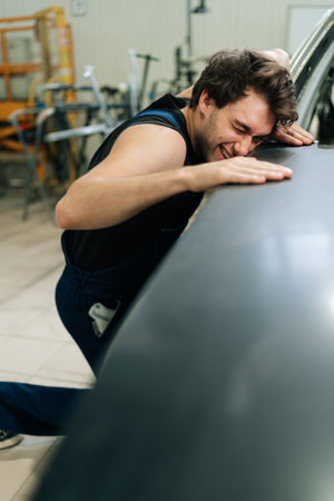Vertical shot of repairman conducts check inspection of car body after polishing surface. Closeup of auto mechanic male checking polished car hood well in workshop. Concept of professional car repair.の写真素材
