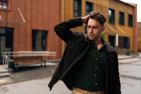 Portrait of confidence young man in trendy attire adjusting hair while walking down street, radiating confidence and urban charm, showcasing modern and fashionable lifestyle.の写真素材