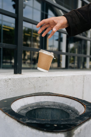 Unrecognizable person tossing disposable coffee cup into public trash can, encouraging responsible waste disposal and promoting urban cleanliness vibrant city setting, environmental consciousness.の写真素材