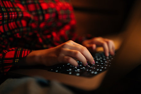 Close-up cropped shot of unrecognizable preteen girl wearing red and black checkered shirt typing on...