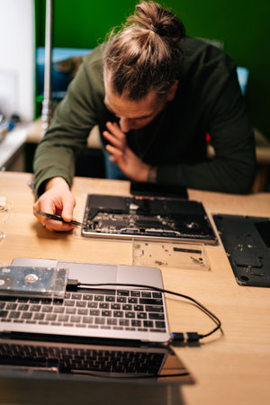 Vertical portrait of technician using tweezers repairing laptop motherboard components in professional electronic workshop setting. Concept of computer hardware, repairing, upgrade, technologyの写真素材