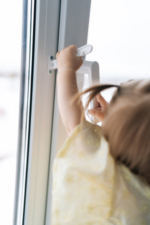 Vertical cropped shot of curious child girl holding touching toward window handle. Concept of...