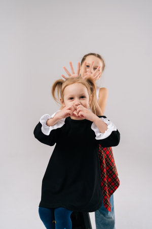 Playful young sisters posing together, sharing lighthearted moments in professional studio setting with white isolated background, expressing joyful connection through animated facial expressions.の写真素材