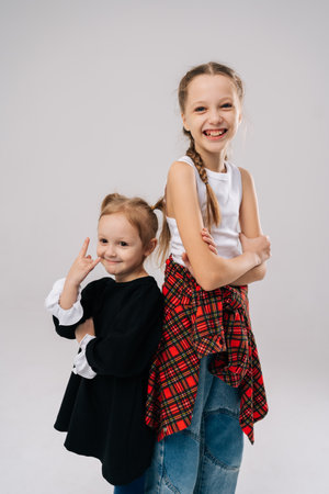 Cheerful two young sisters standing back to back in professional studio with white isolated background, creating heartwarming portrait that captures playful personalities and strong bond.の写真素材