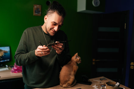 Happy computer technician carefully examining damaged motherboard in electronics repair workshop, accompanied by attentive ginger cat. Concept of intersection of technology and companionship.の写真素材