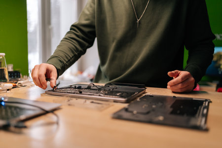 Cropped shot of electronic engineer using tweezers, fixing components on laptop motherboard, performing maintenance and troubleshooting in repair workshop. Concept of computer hardware, repairing.の写真素材