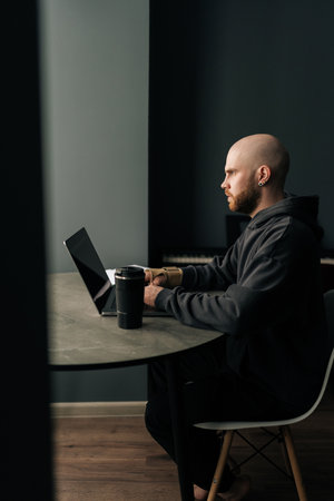 Vertical shot of focused freelancer with wrist brace working on laptop computer at home, enjoying...