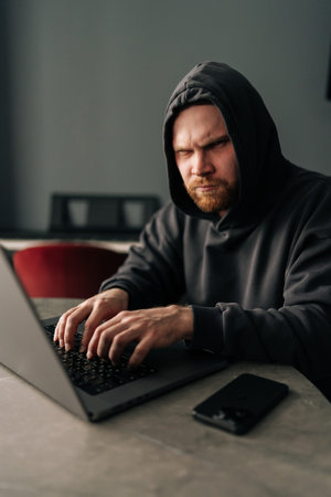 Vertical portrait of male in black hoodie looking at camera while typing on laptop keyboard.の写真素材