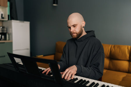 Concentrated male musician playing on electric piano, composing music at home, practicing and recording new song in stylish modern apartment setting. Concept of recording music at home.の写真素材