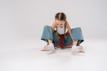 Cheerful 10 years old girl with braided hair wearing white tank top and red plaid shirt, crouching low and balancing on hands and feet in breakdancing pose in studio with white isolated background.の写真素材