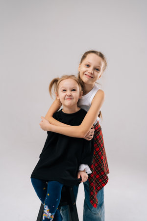 Joyful two young sisters posing for studio portrait, with older sister affectionately hugging younger sister from behind, both smiling happily looking at camera. Concept of happy sisterhood and familyの写真素材