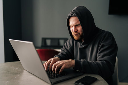 Male wearing black hoodie concentrating looking to screen while typing on laptop keyboard.の写真素材