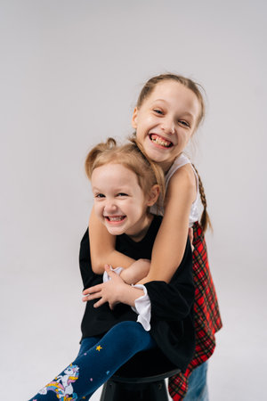 Cheerful sisters hugging and sharing joyful moment, capturing genuine familial bond inside bright professional photography studio with white isolated background. Concept of happy sisterhood and familyの写真素材
