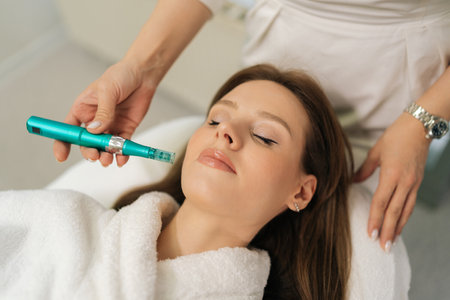 Close-up top view of aesthetician doctor performing microneedling treatment on female client face...