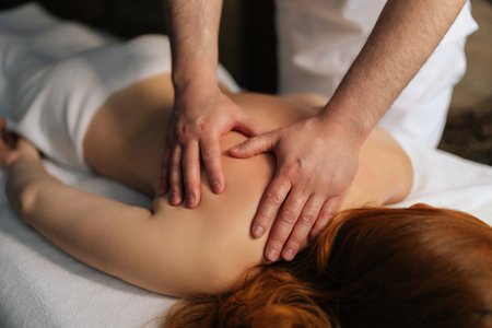 Close-up hands of unrecognizable professional masseur working on female client back, doing therapeutic massage targeting muscle tension and promoting wellness in tranquil spa environment.の写真素材