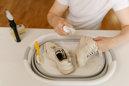 High-angle view of cleaning white sneakers with scrubbing brush and detergent, removing stubborn stains from footwear in basin, preserving shoe hygiene and appearance thorough washing work.の写真素材