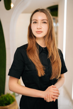 Vertical portrait of confident young female nurse wearing black uniform standing in modern clinic interior looking at camera, exuding professionalism and expertise in healthcare and patient care.の写真素材