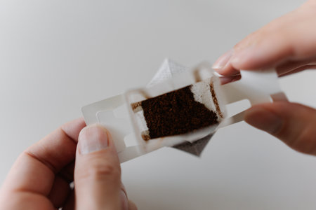 Top view of male hands carefully placing drip coffee bag into transparent glass cup, getting ready to brew fresh cup of coffee in modern kitchen setting at home in morning during breakfast, close-up.の写真素材