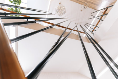 Low-angle view of modern staircase with metal railings and warm wooden handrail, creating striking contrast in contemporary interior illuminated by spherical chandeliers, no people, nobody.の写真素材