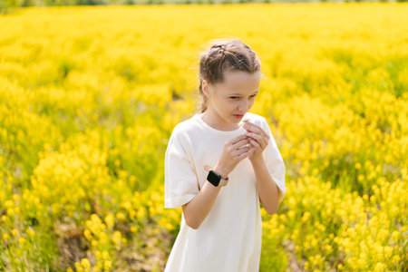 Happy young girl in flowing white dress, joyfully smelling vibrant yellow flowers while basking in warm sunshine of summer day, embracing scents of nature. Concept of happy childhood and recreation.の写真素材
