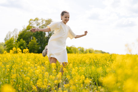 Happy little girl in white dress running joyfully through vibrant field of yellow flowers, embracing warmth of sunny summer day reveling in nature beauty and freedom. Concept of outdoor recreation.の写真素材