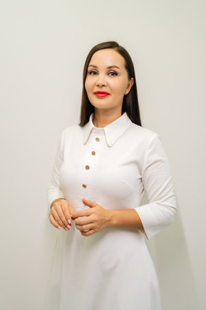 Vertical portrait of brunette female doctor in white uniform and red lipstick, standing on white isolated background, smiling looking at camera, radiating medical expertise and skincare knowledge.の写真素材
