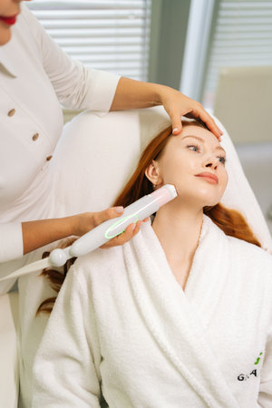 Close-up vertical portrait of beautiful woman receiving microneedling rejuvenation treatment in clinic of aesthetic medicine. Cosmetologist performing needle mesotherapy on female client face.の写真素材