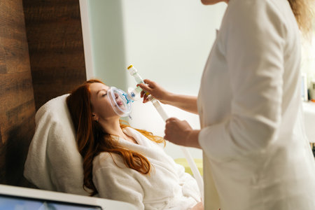 Skilled physician helping putting on oxygen mask for respiratory training to female patient during...