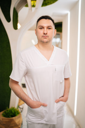 Vertical portrait of professional male masseur standing confidently with hands in pockets looking at camera inside modern spa center, representing wellness and body care expertiseの写真素材