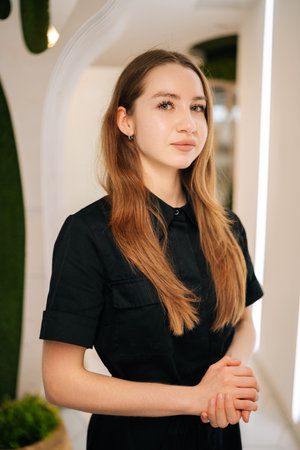 Confident young female nurse wearing black uniform standing posing looking at camera in modern clinic interior, exuding professionalism and showcasing expertise in healthcare and patient careの写真素材