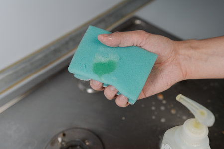 A person is squeezing liquid cleaner from a bottle onto a sponge, preparing to clean a dirty surface, emphasizing domestic chores and hygiene.の写真素材