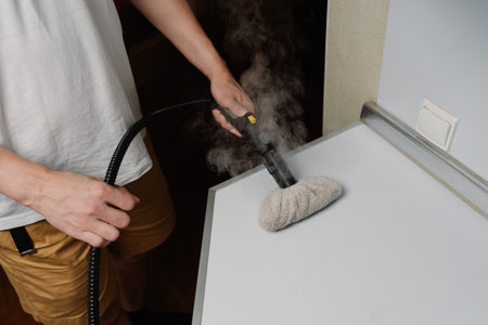 Homeowner male using steam cleaner, sanitizing kitchen countertop with modern housekeeping appliance, maintaining pristine hygiene. Concept of hygiene and cleanliness in domestic environment.の写真素材