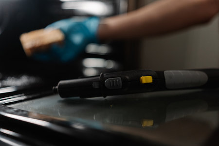 Selective focus of cleaning service employee in blue gloves using steam cleaner and sponge to clean interior of dirty gas oven, ensuring hygiene and maintenance. Concept of hygiene and cleanliness.の写真素材