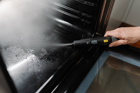 Cleaning company worker male using steam cleaner to remove grease and grime from inside surface of gas oven, ensuring spotless and hygienic kitchen appliance. Concept of housekeeping domestic life.の写真素材