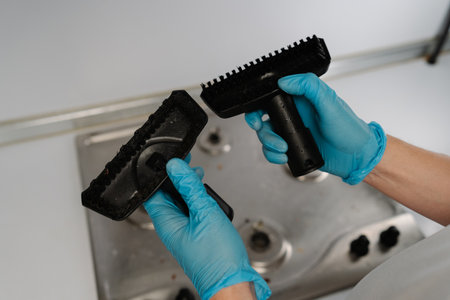 Top view of professional cleaner in rubber gloves holding and comparing two different brushes for steam cleaning dirty stainless steel stovetop, evaluating options for effective appliance maintenance.の写真素材