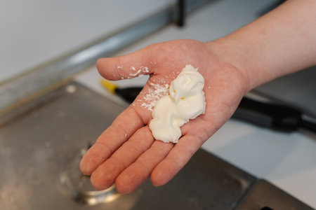 Man holding moisturizing cream mixed with some white powder in hand, preparing skin treatment standing in kitchen setting, close-up. Concept of healthy lifestyle after household cleanliness.の写真素材