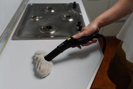 Professional cleaning service employee wiping kitchen countertop with sanitizing steam cleaner near stovetop, maintaining spotless domestic hygiene. Concept of maintenance modern home appliance.の写真素材