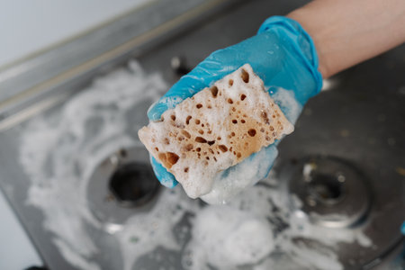 Top view of cleaning company worker in gloves squeezing soapy water from sponge during cleaning dirty gas stove, to removing stubborn grime and grease. Concept of domestic work and household.の写真素材
