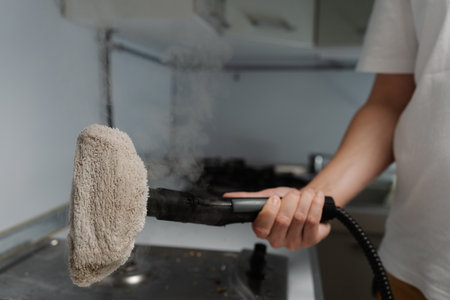 Close-up of unrecognizable housewife male holding steam cleaner with cloth attachment preparing to cleaning dirty gas stove in kitchen, ensuring hygiene and cleanliness, closeup cropped shot.の写真素材