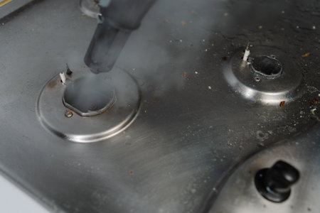 Close-up steam cleaning gas stove surface, eliminating burned food and grease, restoring kitchen surface to pristine condition with sanitizing process. Concept of modern housekeeping appliance.の写真素材