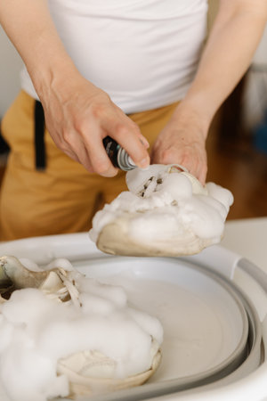 Close-up vertical cropped shot of housewife washing dirty white sneakers with cleaning foam and brush in basin, applying detergent on footwear, doing housework and chores, close-up.の写真素材