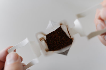 Close-up top view of male hands carefully placing drip coffee bag into transparent glass cup, getting ready to brew fresh cup of coffee in modern kitchen setting at home in morning during breakfast.の写真素材