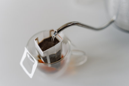 Close-up of hot water pouring from kettle into drip coffee bag placed in glass cup, offering simple and convenient way to brew fresh cup of coffee. Concept of quick way to enjoy fresh cup of coffee.の写真素材